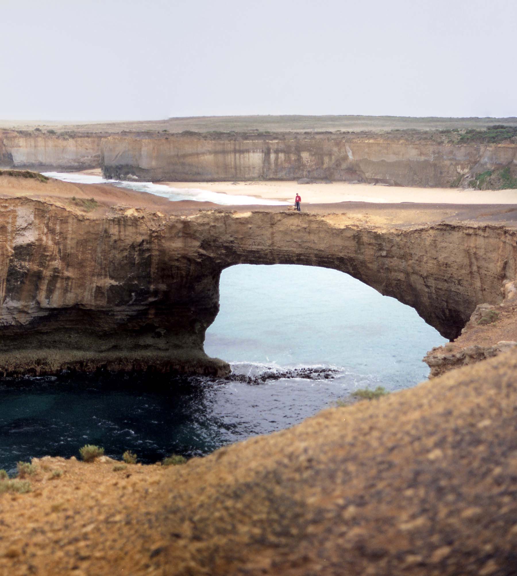 View of a tourist in Nebraska Huskers sweatshirt on top of the London Bridge at Port Campbell National Park.