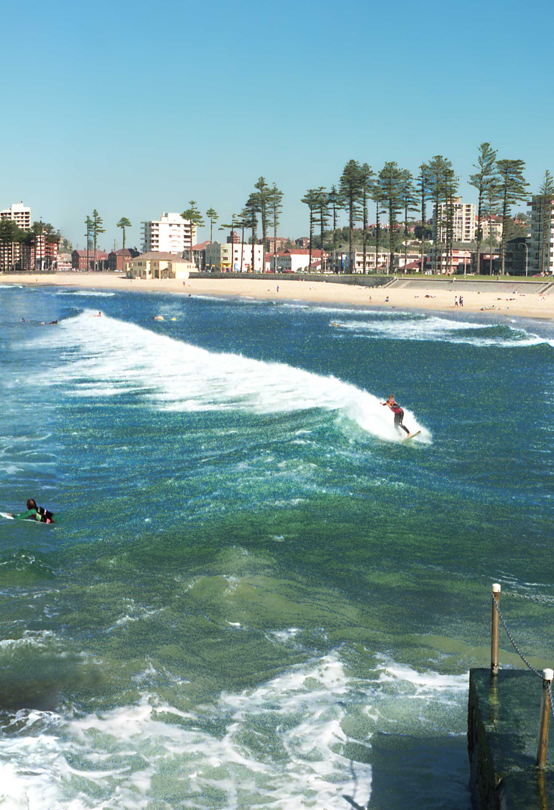 View of surfers in wetsuits catching waves at Manly Beach.